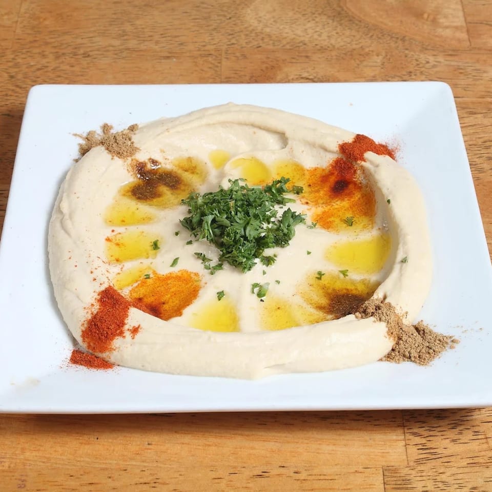 Creamy hummus drizzled with olive oil, paprika, cumin, and fresh parsley on a white plate.