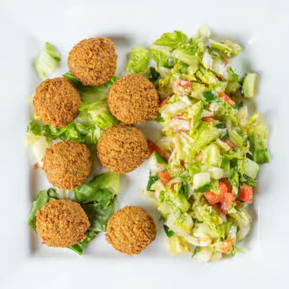 Seven falafel balls and a fresh salad with lettuce, cucumbers, and tomatoes on a white plate.