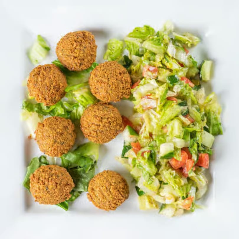 Seven falafel balls and a fresh salad with lettuce, cucumbers, and tomatoes on a white plate.